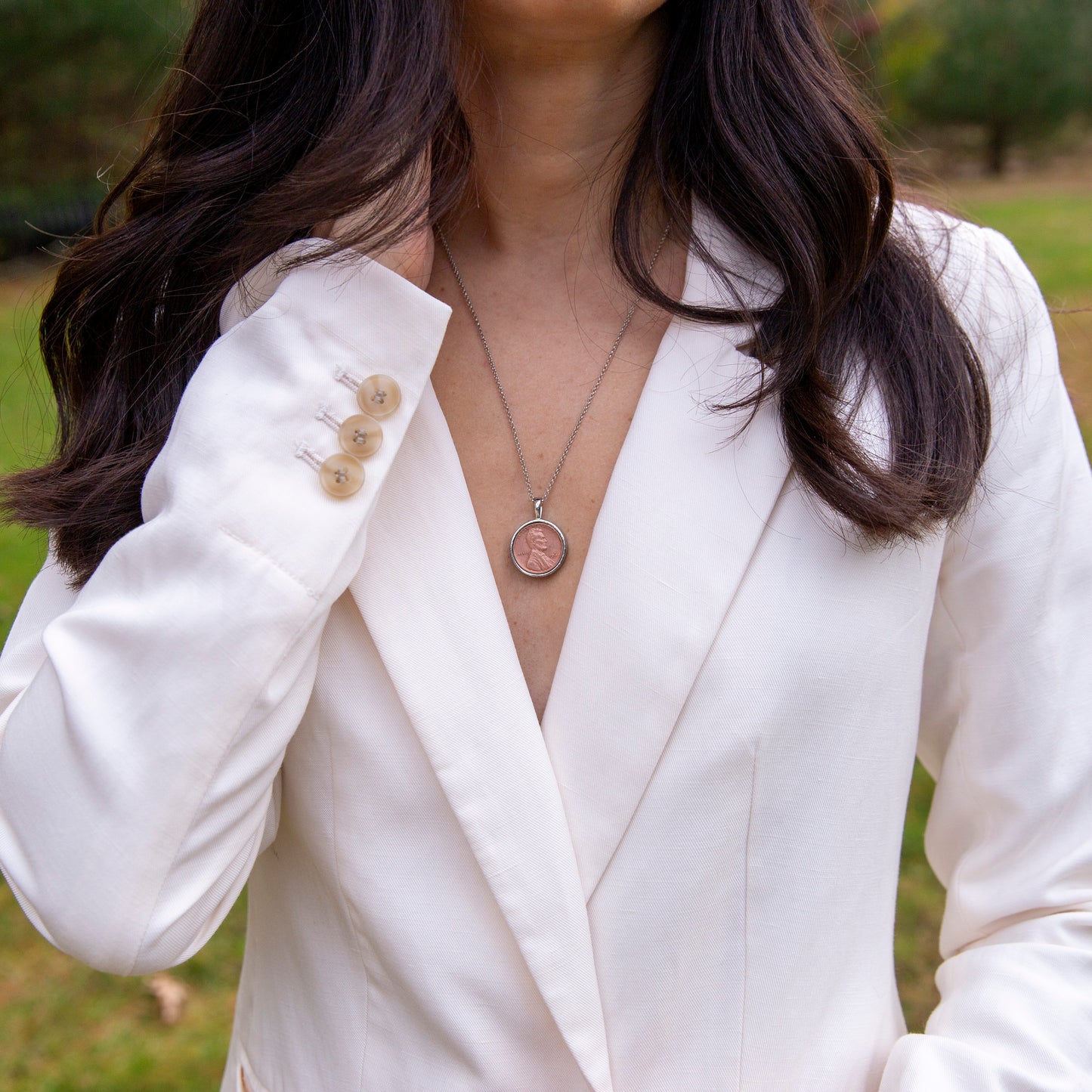 Model is wearing a white jacket and a silver lucky penny necklace.