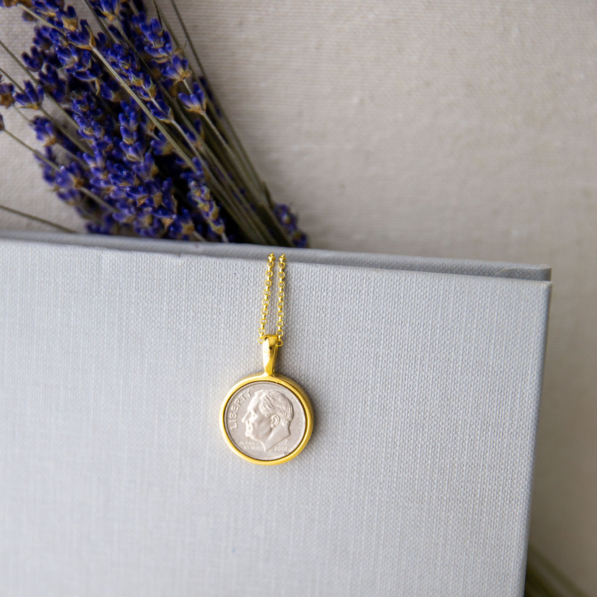 Lucky Dime Personalized Necklace in Gold resting on a book